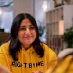 Kvinna med mörkt utsläppt hår med gul college tröja med texten Right by Me