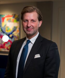 Magnus Oskarsson DLA Piper. Mörk kostym, vit skjorta och mörkblå slips. Kort ljusbrunt hår i sidbena.