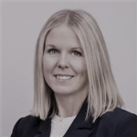 Porträtt av en kvinna med axellångt blont hår, klädd i en mörk kavaj, leende mot kameran.