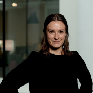 Kvinna med mörkt uppsatt hår och svart topp ler mot kameran.