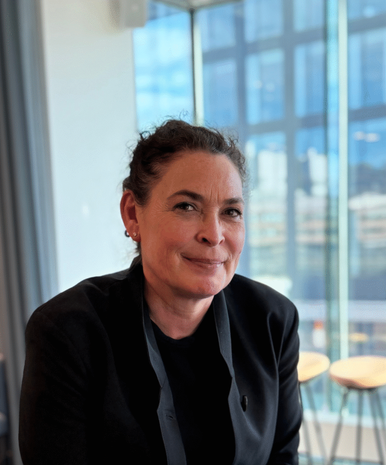 Porträttbild på kvinna med uppsatt hår och mörka kläder som står och kollar mot kameran.