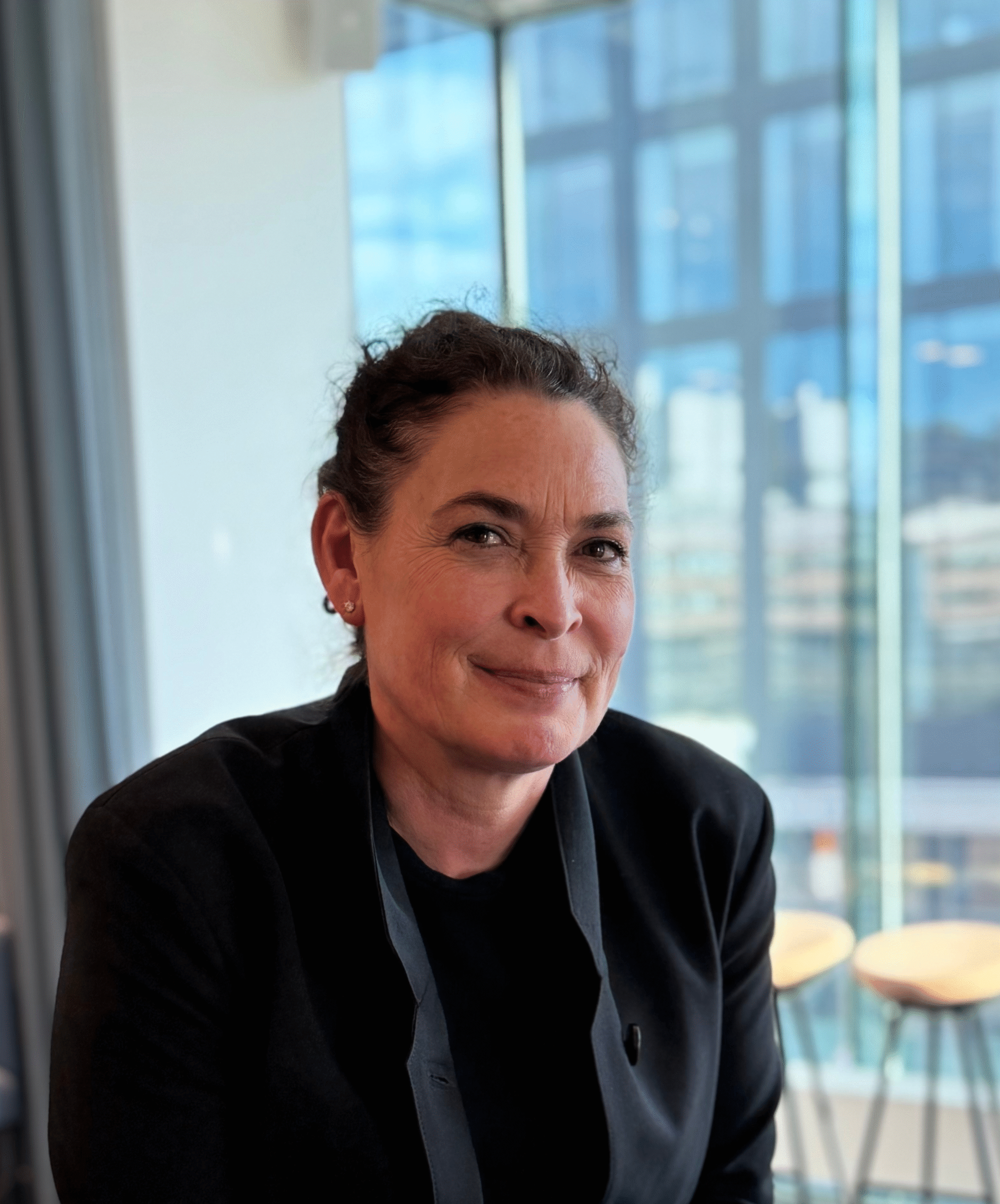 Porträttbild på kvinna med uppsatt hår och mörka kläder som står och kollar mot kameran.