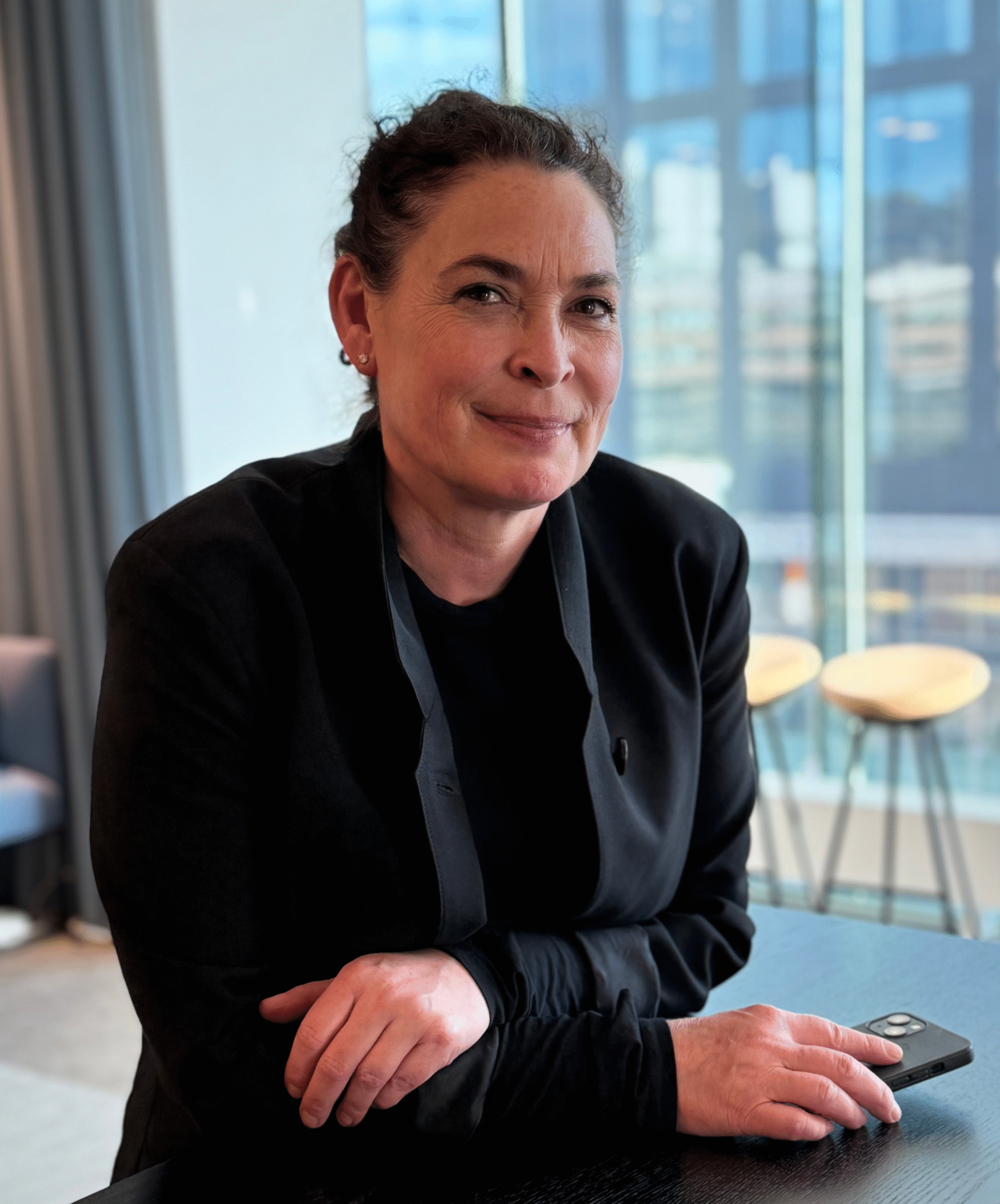 Porträttbild på kvinna med uppsatt hår och mörka kläder som står och kollar mot kameran.