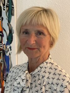 Porträtt på kvinna med ljust kort hår som ler mot kameran. Hon har en vit blus på sig med svart mönster.