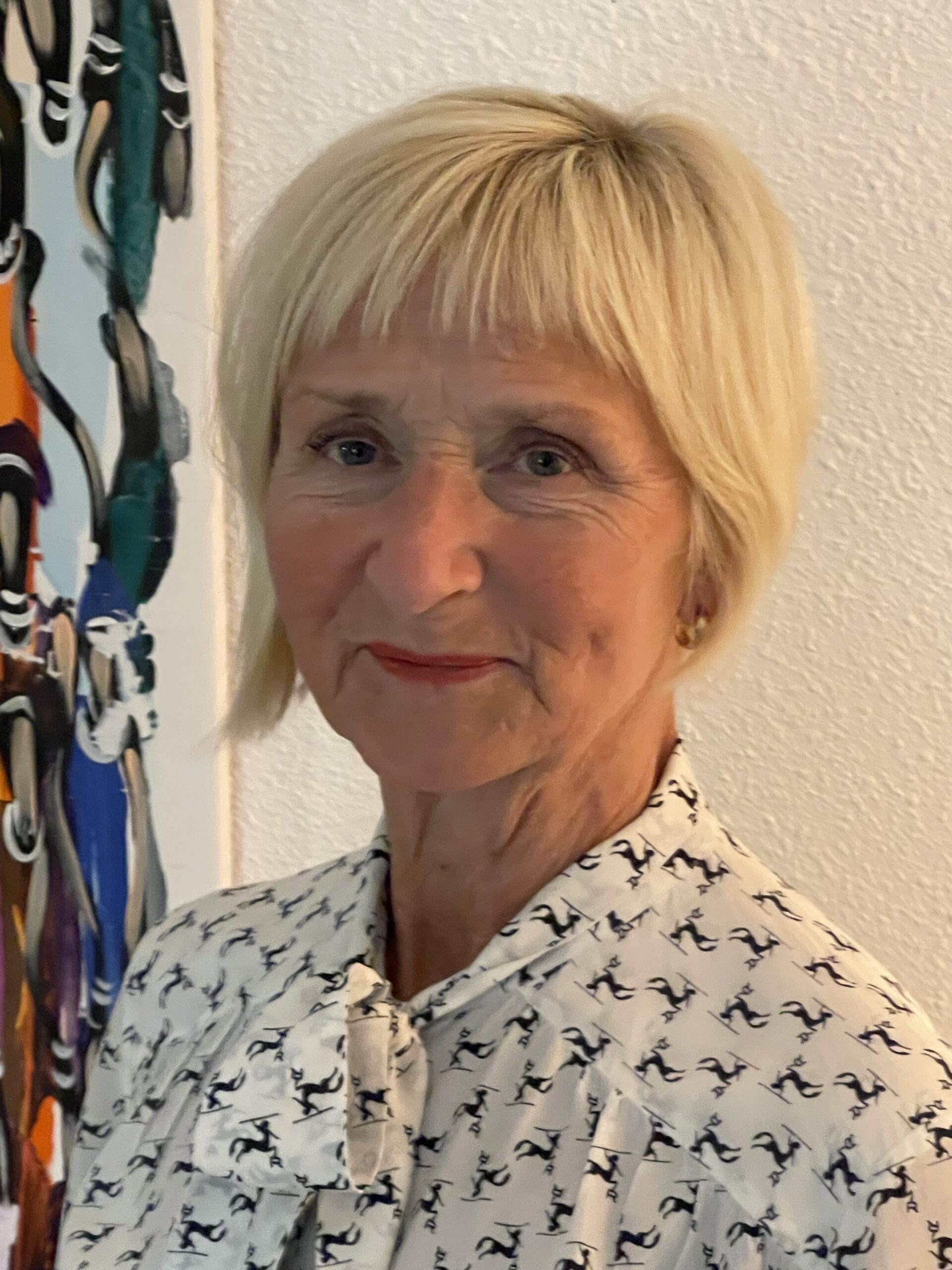 Porträtt på kvinna med ljust kort hår som ler mot kameran. Hon har en vit blus på sig med svart mönster.