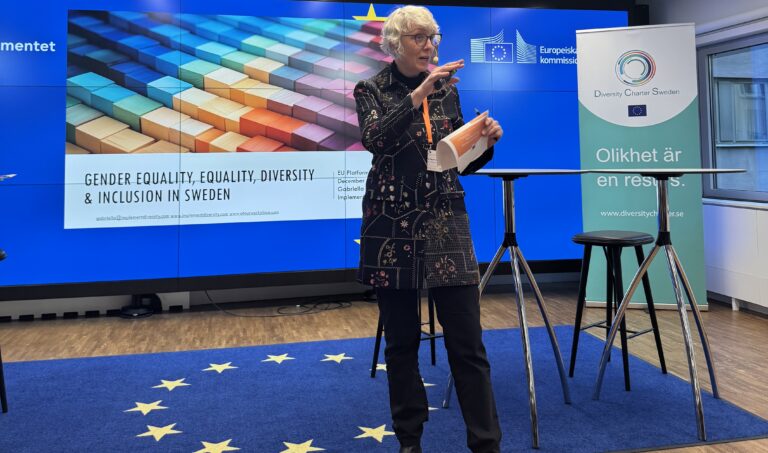 Kvinna med svarta kläder och grått hår håller i ett föredrag.