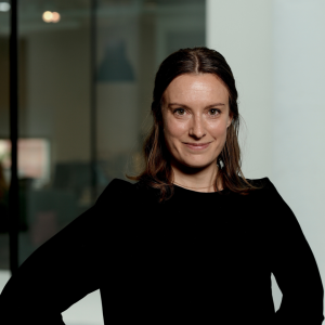 Kvinna med mörkt uppsatt hår och svart topp ler mot kameran.