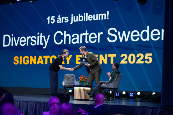 På scen under Signatory Event 2025. Victor Frisk, Måns Liljenlov och Hanna Wallensten hälsar på varandra. Publi i förgrunden.